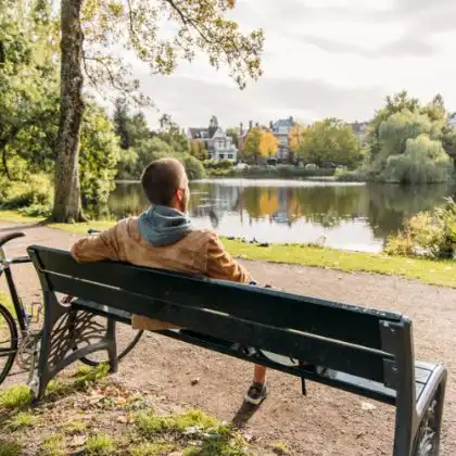 Homem sentado em banco de frente para lago