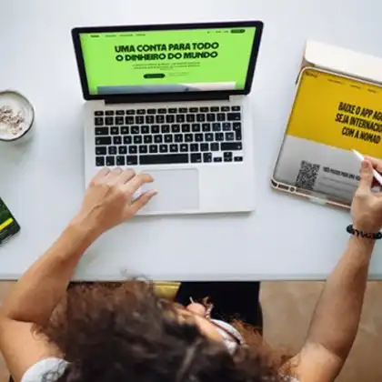 Mulher analisa os sites da Wise pelo computador, da Nomad pelo tablet e do C6 Bank no celular