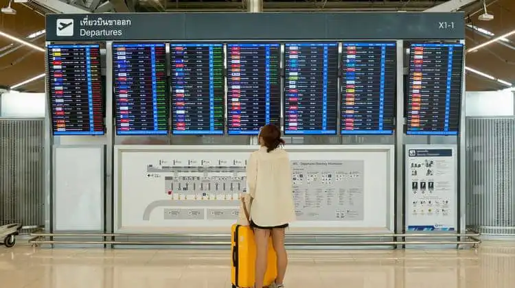 Mulher procurando seu voo diante de quadro em aeroporto