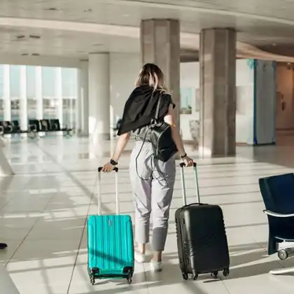 Mulher caminhando no aeroporto com duas malas para saber quanto custa uma mala extra em voo internacional