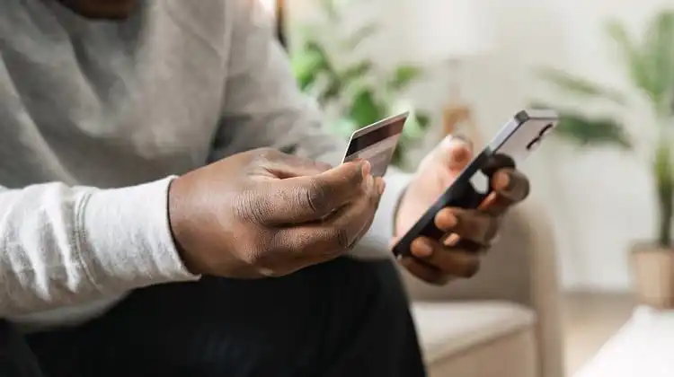 Homem negro segurando celular e cartão de crédito