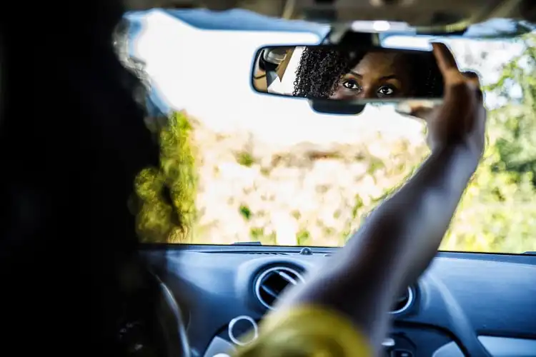 Mulher ajustando espelho retrovisor de carro.