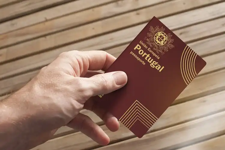 Uma mão segura um passaporte português e uma placa de madeira ao fundo