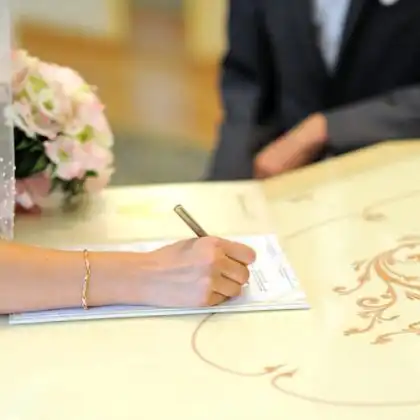 Noiva assinando a certidão de casamento com marido próximo.