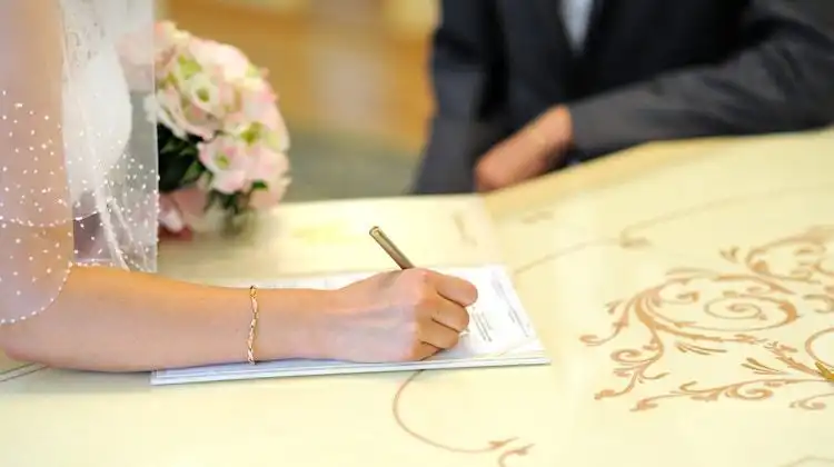 Noiva assinando a certidão de casamento com marido próximo.