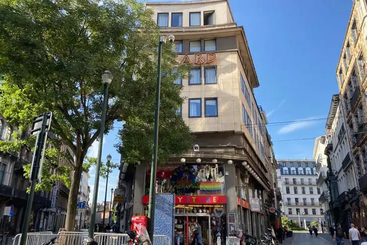 Praça em Bruxelas, com bandeira LGBTQIA+ estendida no topo de uma loja.