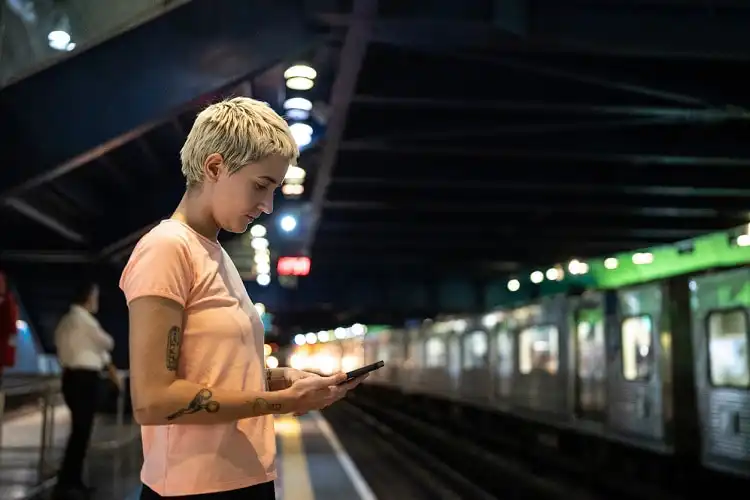 Mulher em estação de trem, checando o celular.