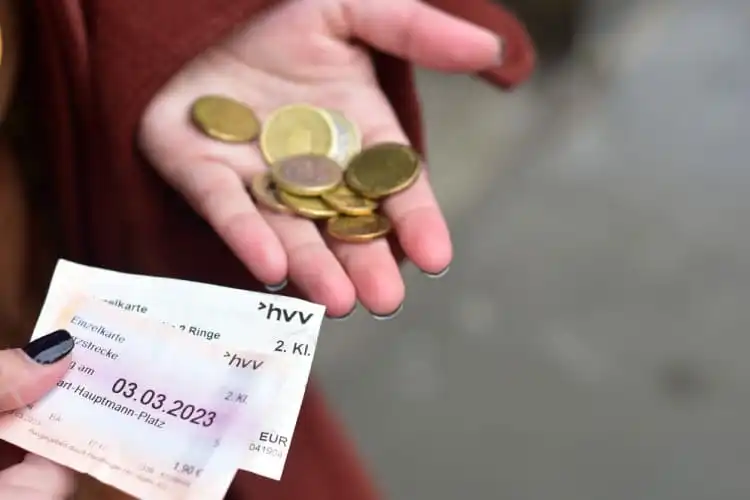 Pessoa segurando nas mãos moedas e ticket de transporte público
