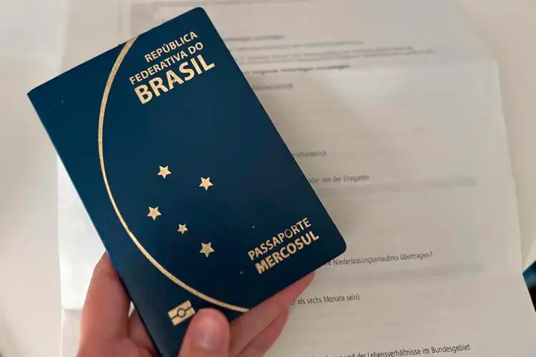 Passaporte brasileiro e papel com a lista de documentos para o visto de férias trabalho na Alemanha.