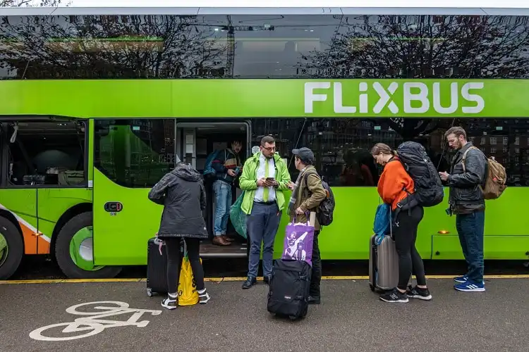 Funcionário da Flixbus em frente ao ônibus, com pessoas em fila esperando para embarcar.