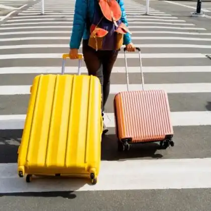Mulher atravessa rua puxando mala de mão e mala de despachar