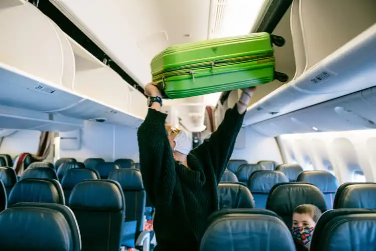 Mulher colocando bagagem de bordo na cabine do avião