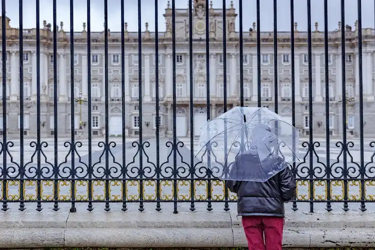 Mulher olhando para a fachada do palácio real, em Madrid, em dia chuvoso