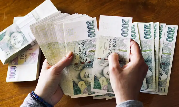 Mulher contando notas que fazem parte da moeda da República Tcheca