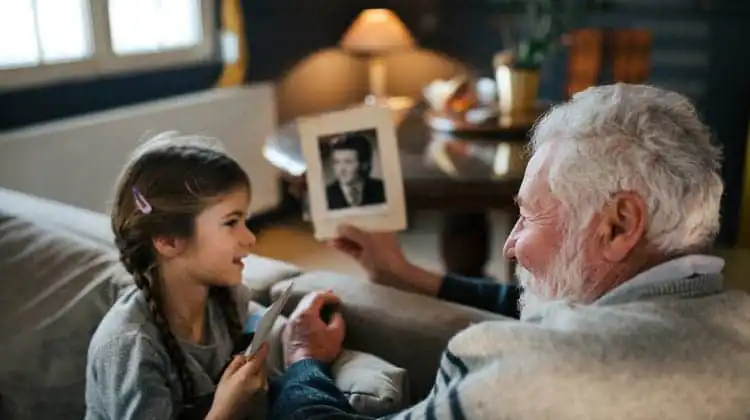 Avô sentado com a neta mostrando uma fotografia antiga e conversando sobre nomes e sobrenomes alemães.