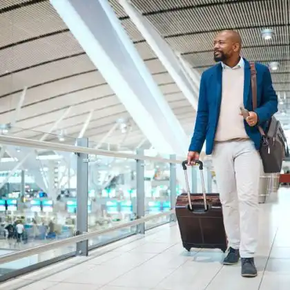 Homem caminhando no aeroporto com mala e passagem aérea para Londres executiva nas mãos.