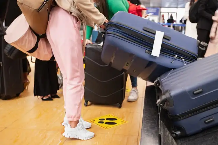 Mulher retirando malas de esteira do aeroporto.