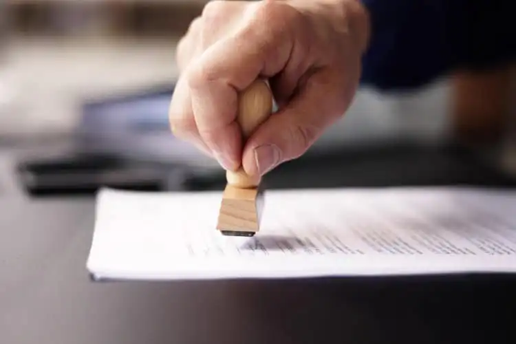 Pessoa carimbando um documento em cima de mesa