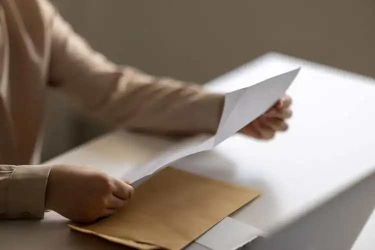 Pessoa abrindo uma carta enttregada em um envelope amarelo