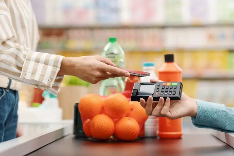 Mulher pagando compras com cartão no supermercado após receber salário mínimo na Inglaterra. 