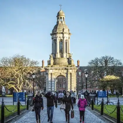 Estudantes em frente a Trinity College em dia ensolarado em Dublin.