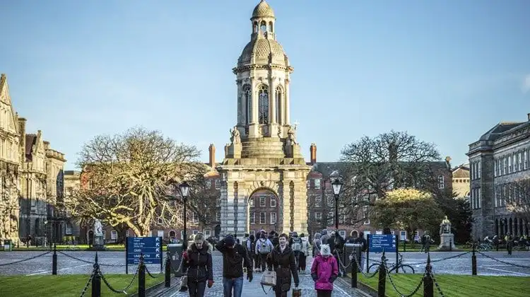 Estudantes em frente a Trinity College em dia ensolarado em Dublin.