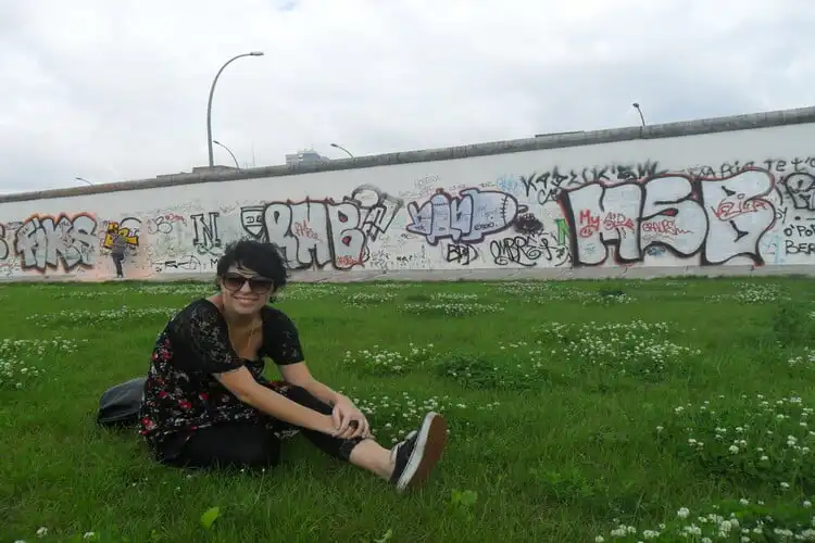 roberta schmoi sentada em frente a parte traseira do muro de berlim