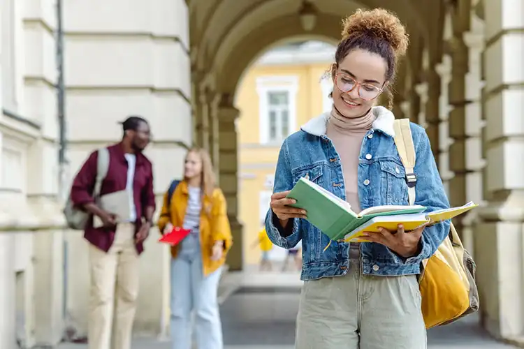 Jovem estudante com bolsa de estudo na Alemanha lendo um livro em frente a universidade.