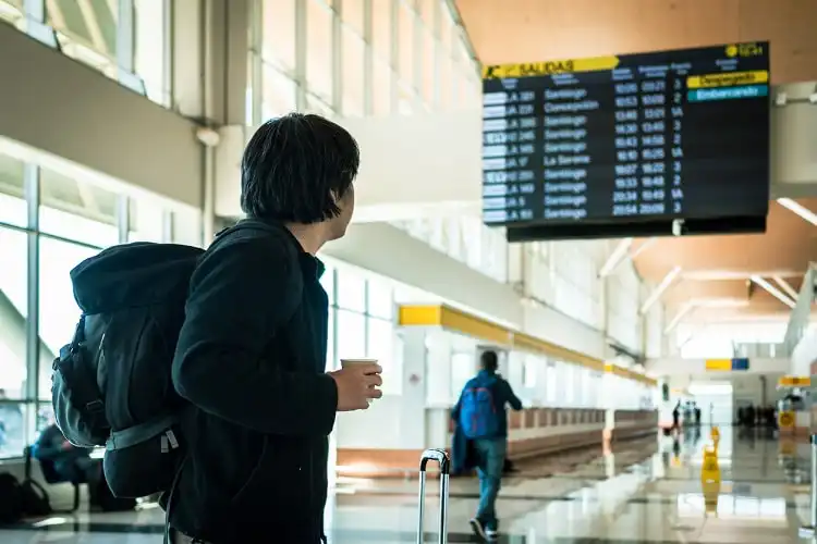 Homem jovem em aeroporto, olhando painel de aeroporto