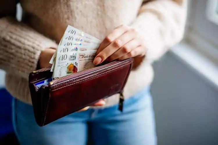 Mulher tirando libras esterlinas da carteira para pagar contas de morar na Inglaterra. 