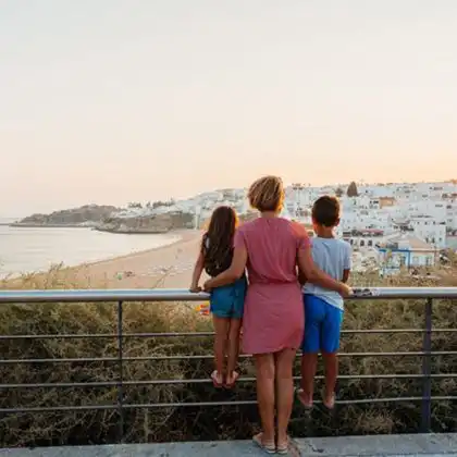 Mãe com dois filhos observam o pôr do sol em cidade de Portugal