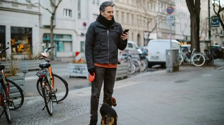 Homem na rua parado ao lado do seu cachorro.