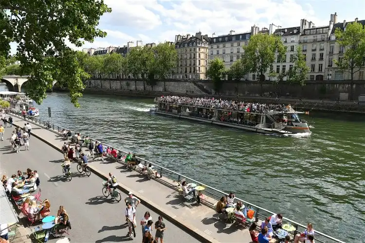 Pessoas na rua em Paris e um barco com turistas no Rio Sena