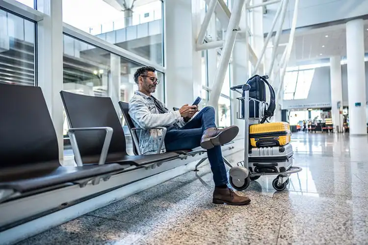Homem com celular em sala de espera do aeroporto