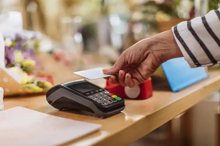 Mãos femininas aproximando um cartão de uma máquina de crédito