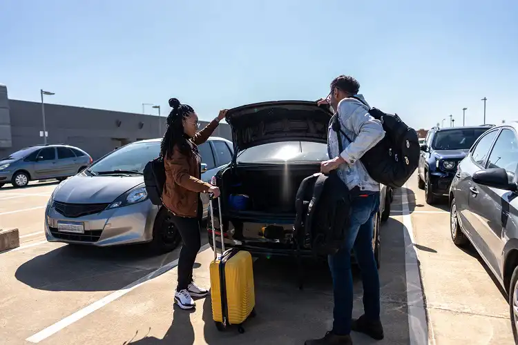 Homem e mullher abrindo porta malas de carro.