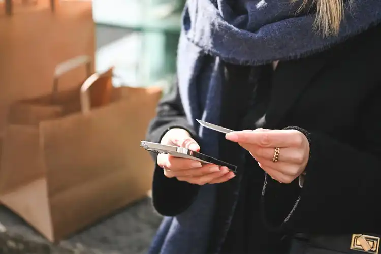 Mulher segura cartão de compras e celular.