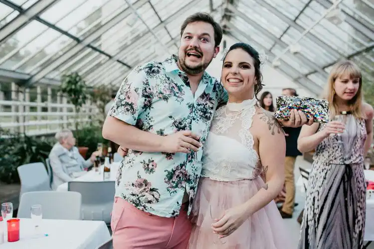 amigos em festa de casamento em estufa. ela com saia rosa e top branco e ele com camisa floral e calça rosa. mudar de país é também enfrentar perdas ao morar no exterior.