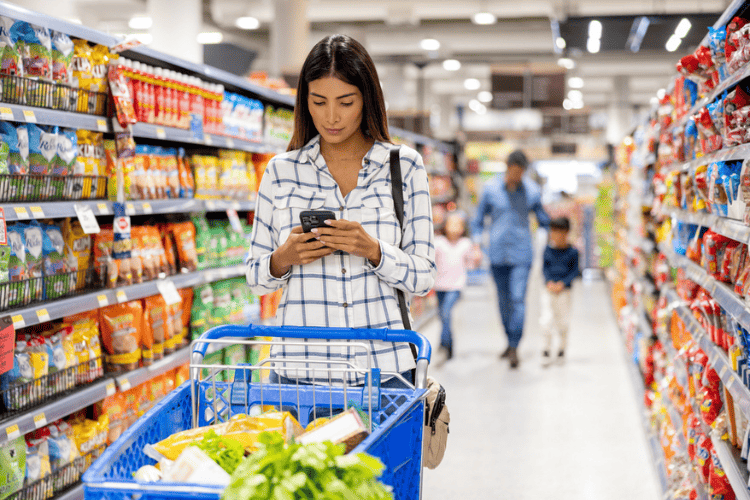 Mulher em supermercado verifica aplicativos para fazer compras