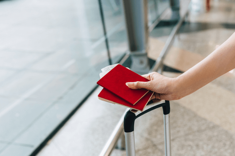 Pessoa segurando passaporte próximo a mala