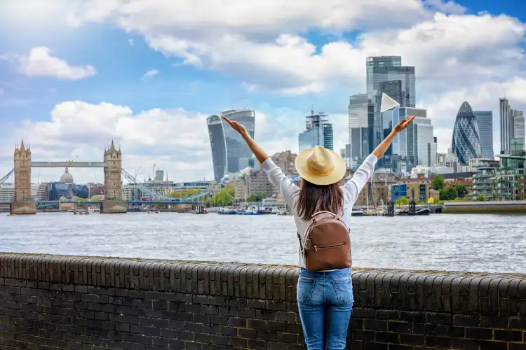 Mulher de braços abertos com cidade de Londres ao fundo.