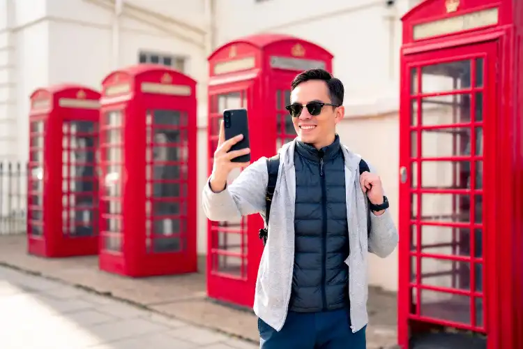 Homem tirando foto no celular em frente a cabine em Londres.