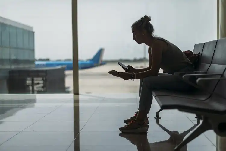 Jovem em aeroporto, olhando o celular.