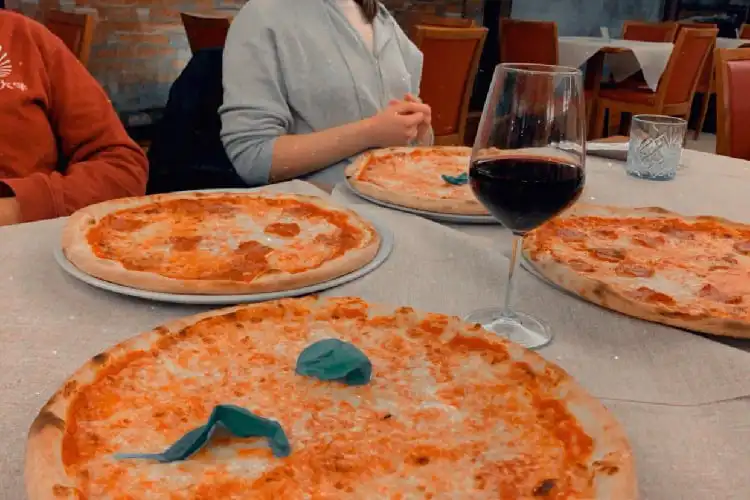Pessoas comendo pizza italiana e bebendo um vinho.