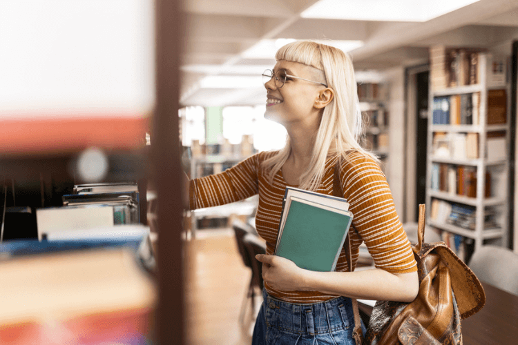 Jovem procurando livros em estante na biblioteca.