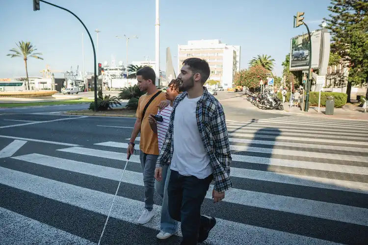 Três turistas entre eles um deficiente visual atravessam rua na Europa
