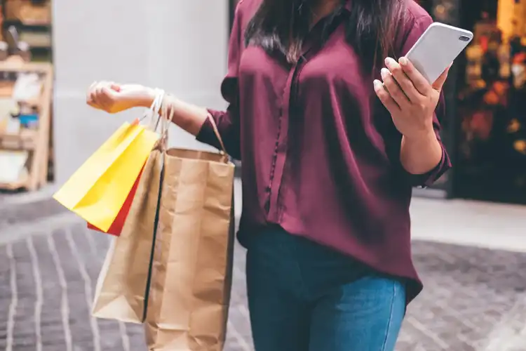 Jovem segurando sacolas e smartphone