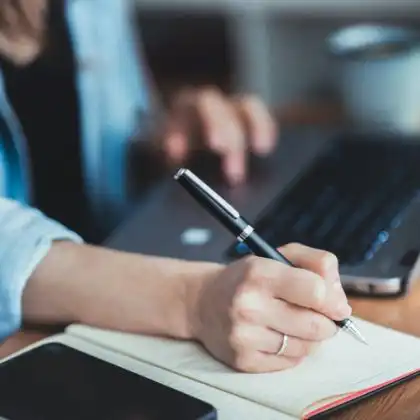 Mulher no laptop e fazendo anotações no caderno