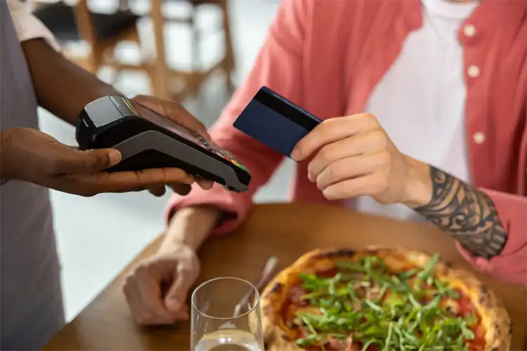 Jovem pagando por uma pizza com cartão de crédito ou débito