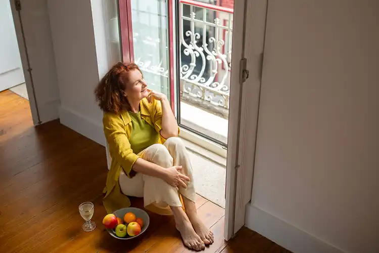 Mulher sentada em frente à janela de um apartamento vazio